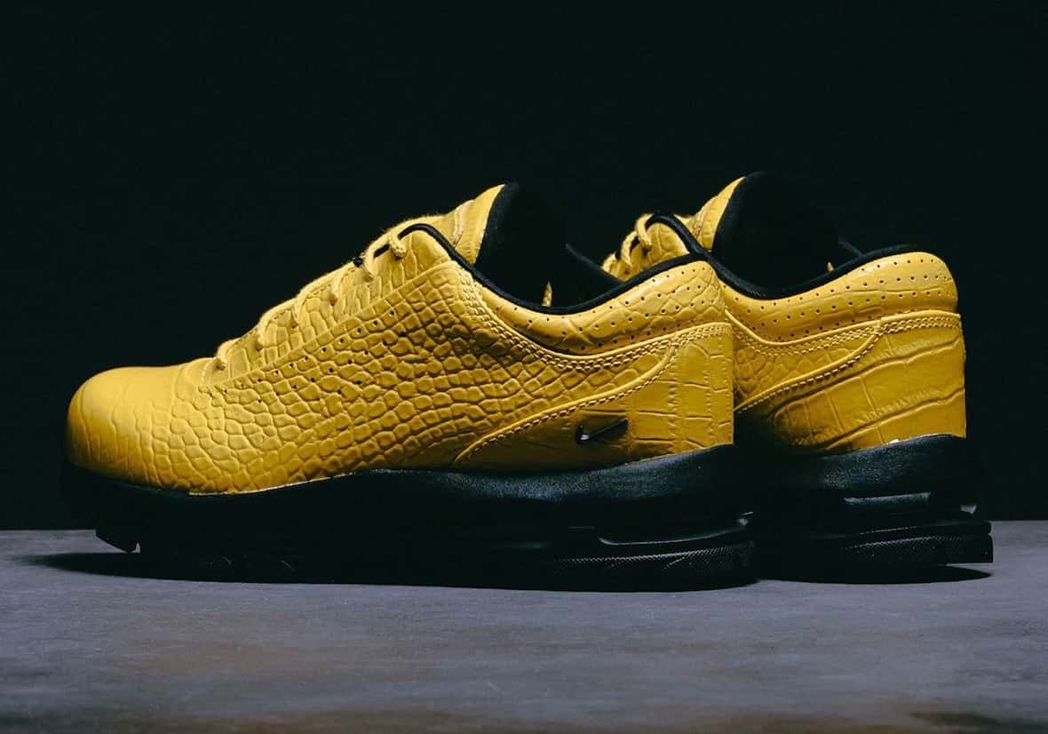 Par del Nike Air Max Goadome Low Yellow Croc sobre una superficie gris y fondo negro, con upper de cuero amarillo brillante grabado tipo cocodrilo, cordones amarillos, swoosh negro chico en el lateral y base negra con unidades Air visibles